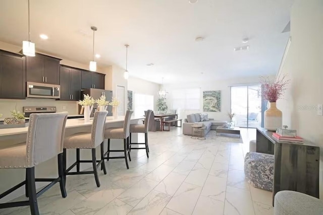 4973 Windermere Ave, Kissimmee, FL 34746 - kitchen featuring appliances with stainless steel finishes, light marble finish floors, a breakfast bar, open floor plan, and light countertops