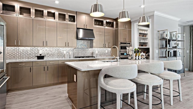 14375 Hammock Oak St, Parrish, FL 34219 - kitchen with under cabinet range hood, ornamental molding, gas stovetop, light wood finished floors, and an island with sink