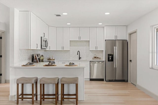 1030 Huntington Ct, Longwood, FL 32750 - kitchen with appliances with stainless steel finishes, tasteful backsplash, a peninsula, light wood-style flooring, and white cabinets