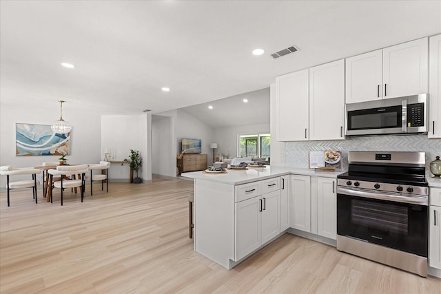 1030 Huntington Ct, Longwood, FL 32750 - kitchen featuring appliances with stainless steel finishes, a peninsula, light wood finished floors, decorative backsplash, and white cabinetry