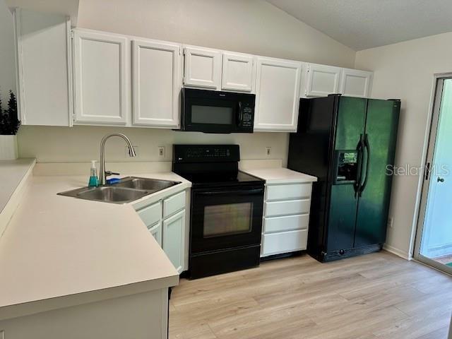 125 Reserve Cir Unit 205, Oviedo, FL 32765 - kitchen featuring black appliances, lofted ceiling, light wood-type flooring, white cabinets, and light countertops