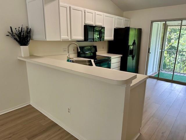 125 Reserve Cir Unit 205, Oviedo, FL 32765 - kitchen featuring black appliances, wood finished floors, vaulted ceiling, light countertops, and a peninsula