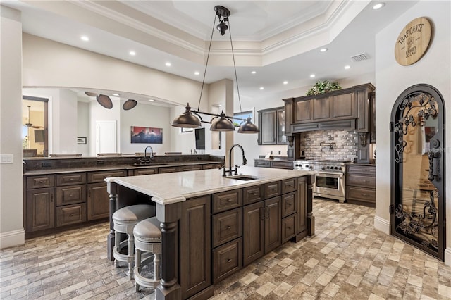 14315 80th Ave, Sebastian, FL 32958 - kitchen featuring stainless steel stove, crown molding, dark brown cabinets, a kitchen island with sink, and tasteful backsplash