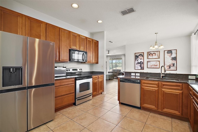 5116 Tempic Dr, Mount Dora, FL 32757 - kitchen with appliances with stainless steel finishes, brown cabinets, a chandelier, dark countertops, and light tile patterned flooring