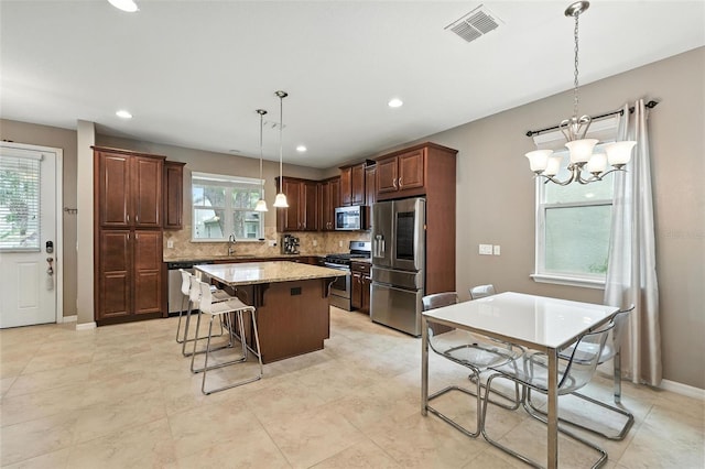 1110 Pine Falls Ln, Ocoee, FL 34761 - kitchen with appliances with stainless steel finishes, a kitchen island, decorative backsplash, a chandelier, and hanging light fixtures