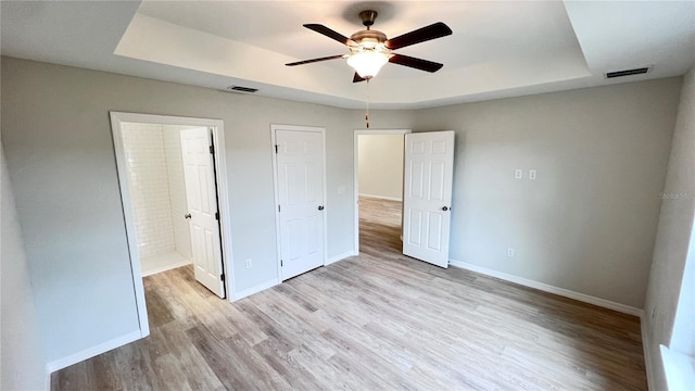 4413 Grass Ave, Sebring, FL 33875 - unfurnished bedroom featuring a raised ceiling, light wood-style flooring, ensuite bath, and a ceiling fan