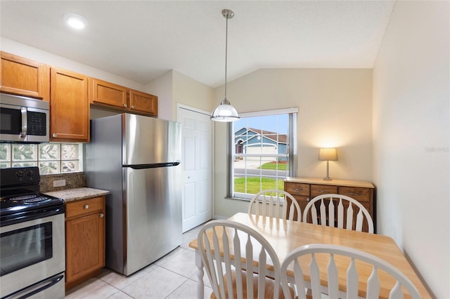 162 Canary Island Cir, Davenport, FL 33837 - kitchen with stainless steel appliances, vaulted ceiling, light tile patterned floors, brown cabinets, and hanging light fixtures