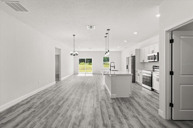 16057 SW 17th Ave, Ocala, FL 34473 - kitchen with stainless steel appliances, white cabinetry, light wood-style flooring, open floor plan, and a textured ceiling