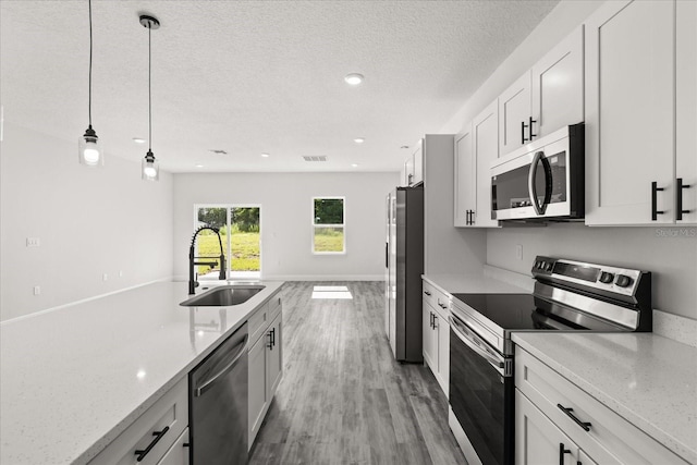 16057 SW 17th Ave, Ocala, FL 34473 - kitchen with appliances with stainless steel finishes, hanging light fixtures, light wood-style flooring, white cabinetry, and a textured ceiling