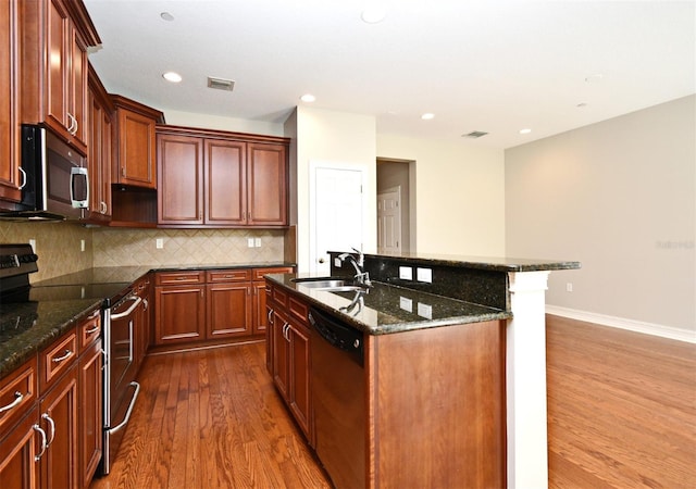 1649 Lake Baldwin Ln, Orlando, FL 32814 - kitchen featuring stainless steel appliances, dark wood finished floors, backsplash, a kitchen island with sink, and dark stone countertops
