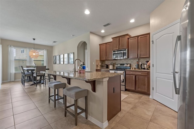 1958 Commander Way, Kissimmee, FL 34746 - kitchen featuring appliances with stainless steel finishes, brown cabinets, tasteful backsplash, a kitchen breakfast bar, and light stone countertops