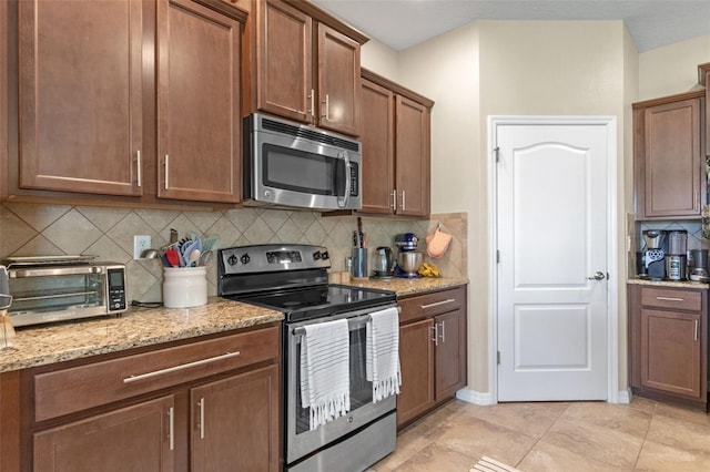1958 Commander Way, Kissimmee, FL 34746 - kitchen with appliances with stainless steel finishes, decorative backsplash, light stone countertops, brown cabinetry, and light tile patterned floors