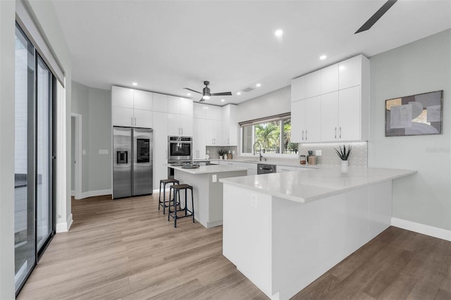 9353 Gotha Rd, Windermere, FL 34786 - kitchen featuring appliances with stainless steel finishes, a ceiling fan, a kitchen breakfast bar, light wood-style flooring, and decorative backsplash