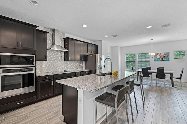 461 Diamond Dove Cv, Winter Springs, FL 32708 - kitchen with appliances with stainless steel finishes, wall chimney range hood, wood finish floors, light stone countertops, and a kitchen bar