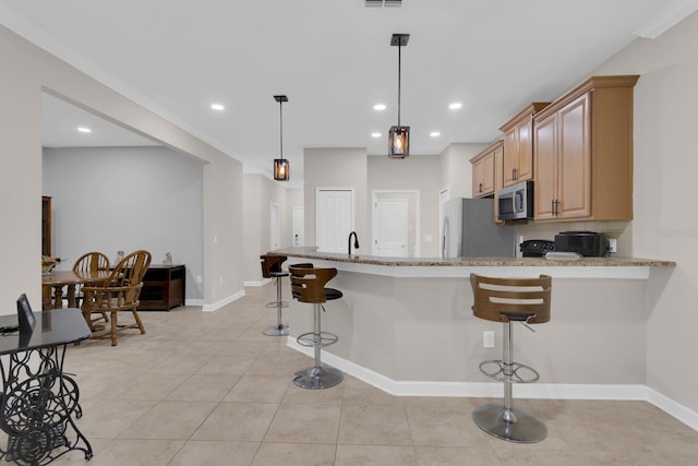 kitchen with freestanding refrigerator, stainless steel microwave, a breakfast bar area, light stone countertops, and recessed lighting