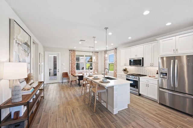 2563 Long Pine Ave, Apopka, FL 32712 - kitchen with stainless steel appliances, a center island with sink, wood finished floors, light countertops, and tasteful backsplash