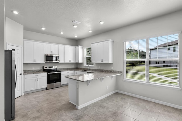 505 Venetian Palms Blvd, New Smyrna Beach, FL 32168 - kitchen with appliances with stainless steel finishes, a peninsula, a textured ceiling, white cabinetry, and light stone countertops
