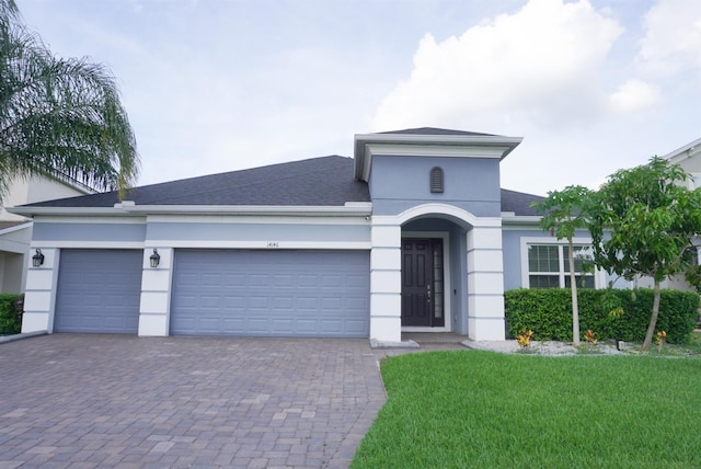 view of front of property featuring stucco siding, decorative driveway, an attached garage, a front yard, and roof with shingles
