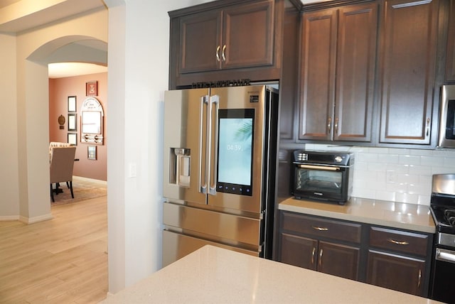 kitchen with stainless steel appliances, arched walkways, light wood-type flooring, tasteful backsplash, and dark brown cabinetry