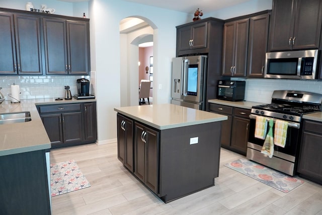 kitchen with appliances with stainless steel finishes, arched walkways, light wood-style floors, and tasteful backsplash