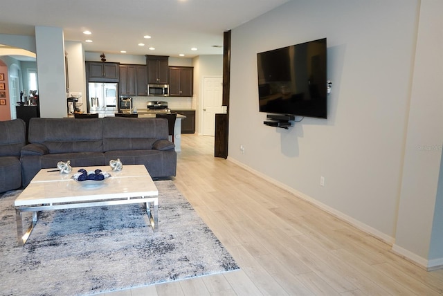 living area with arched walkways, light wood finished floors, and recessed lighting