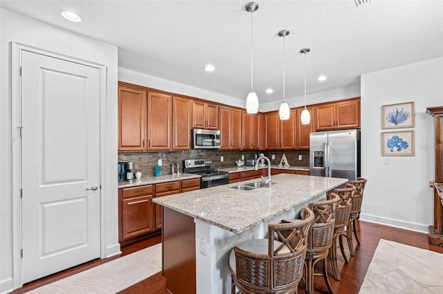 1181 Castlevecchio Loop, Orlando, FL 32825 - kitchen with stainless steel appliances, brown cabinets, decorative backsplash, pendant lighting, and a kitchen island with sink