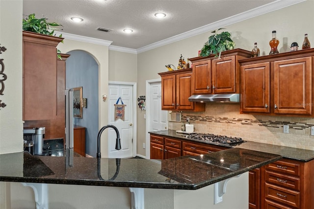 11613 Swift Water Cir, Orlando, FL 32817 - kitchen with under cabinet range hood, ornamental molding, stainless steel gas stovetop, decorative backsplash, and a kitchen bar