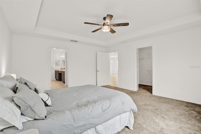 554 Pawnee Ct, Haines City, FL 33844 - bedroom featuring a tray ceiling, a walk in closet, light carpet, ensuite bathroom, and a ceiling fan