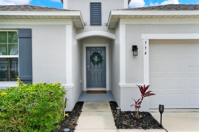 554 Pawnee Ct, Haines City, FL 33844 - view of exterior entry with a garage, stucco siding, and a shingled roof