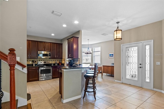 2122 Bent Grass Ave, Ocoee, FL 34761 - kitchen featuring appliances with stainless steel finishes, dark countertops, decorative backsplash, a breakfast bar area, and light tile patterned floors