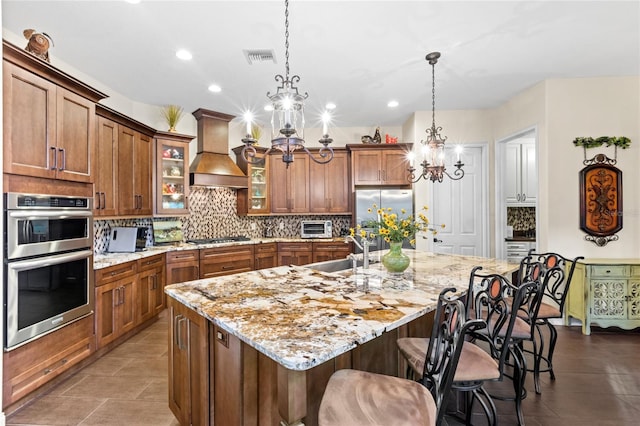 8424 Lake Burden Cir, Windermere, FL 34786 - kitchen with custom range hood, stainless steel appliances, a chandelier, brown cabinets, and backsplash
