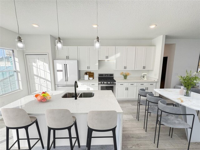 572 W Bluster Pl, Citrus Springs, FL 34434 - kitchen with gas stove, freestanding refrigerator, light wood finished floors, a textured ceiling, and white cabinets