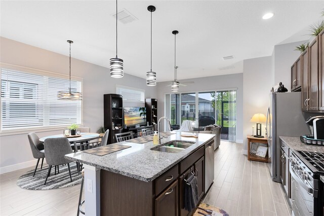 2302 Datura Loop, Saint Cloud, FL 34772 - kitchen featuring appliances with stainless steel finishes, dark brown cabinetry, light stone countertops, an island with sink, and pendant lighting