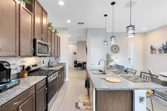 2302 Datura Loop, Saint Cloud, FL 34772 - kitchen featuring appliances with stainless steel finishes, a kitchen bar, decorative backsplash, an island with sink, and light stone countertops