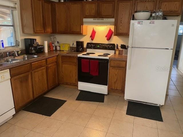 1807 N Powers Dr, Orlando, FL 32818 - kitchen featuring white appliances, under cabinet range hood, brown cabinetry, light tile patterned floors, and dark countertops