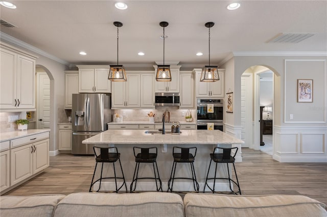 10180 Merrymeeting Bay Dr, Winter Garden, FL 34787 - kitchen featuring appliances with stainless steel finishes, arched walkways, a kitchen bar, ornamental molding, and light wood-style floors