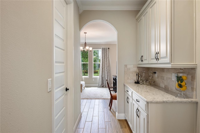 10180 Merrymeeting Bay Dr, Winter Garden, FL 34787 - kitchen featuring crown molding, arched walkways, decorative backsplash, light wood-style floors, and light stone countertops