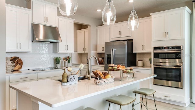 5277 Bowspirit Way, Saint Cloud, FL 34771 - kitchen featuring under cabinet range hood, appliances with stainless steel finishes, white cabinets, backsplash, and a breakfast bar area