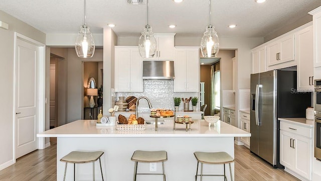 5277 Bowspirit Way, Saint Cloud, FL 34771 - kitchen with exhaust hood, appliances with stainless steel finishes, a kitchen breakfast bar, light wood-type flooring, and decorative backsplash