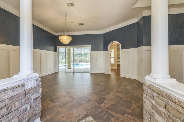 1818 W Cobblestone Ln, Saint Augustine, FL 32092 - unfurnished living room featuring decorative columns, a decorative wall, stone tile flooring, wainscoting, and ornamental molding