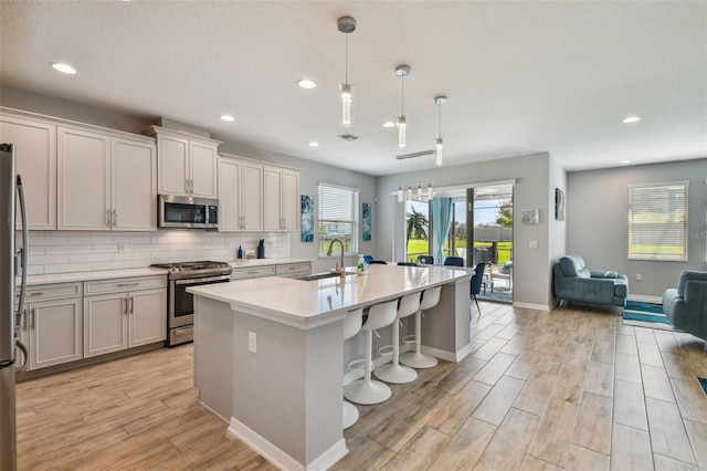 2433 Santa Vista Loop, Apopka, FL 32703 - kitchen with appliances with stainless steel finishes, light wood-style floors, open floor plan, a kitchen island with sink, and light countertops