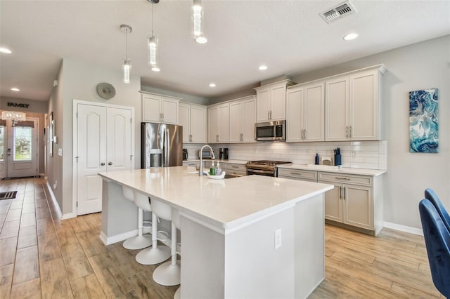 2433 Santa Vista Loop, Apopka, FL 32703 - kitchen featuring appliances with stainless steel finishes, a center island with sink, backsplash, light countertops, and light wood-style floors