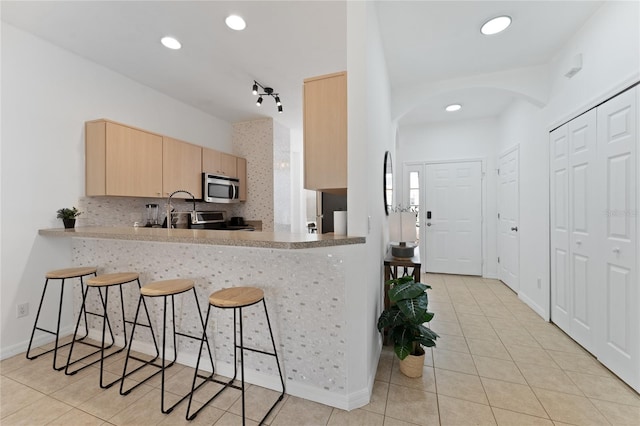 1176 S Beach Cir, Kissimmee, FL 34746 - kitchen with appliances with stainless steel finishes, light brown cabinets, light tile patterned floors, arched walkways, and a breakfast bar area