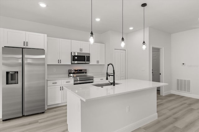 1970 SW 160th Pl, Ocala, FL 34473 - kitchen with appliances with stainless steel finishes, white cabinetry, light wood finished floors, an island with sink, and decorative light fixtures