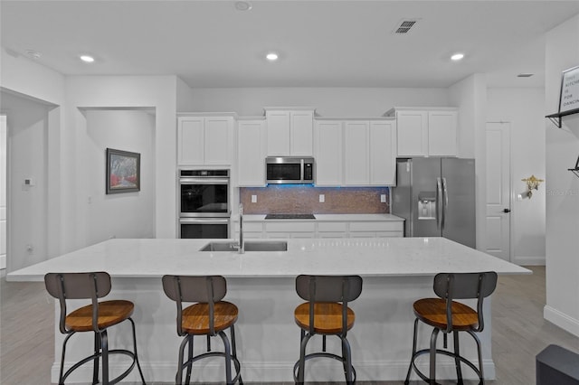 2149 Raglan Cir, Ormond Beach, FL 32174 - kitchen featuring stainless steel appliances, white cabinets, light wood finished floors, tasteful backsplash, and a large island with sink