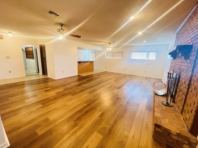 1980 Williams Manor Ave, Orlando, FL 32811 - unfurnished living room with a ceiling fan, a brick fireplace, arched walkways, light wood-style flooring, and a textured ceiling