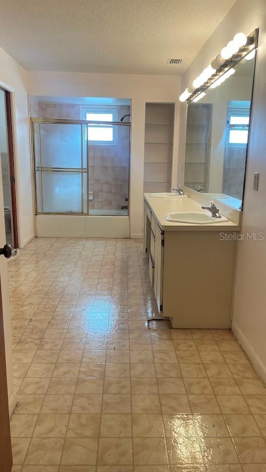 1980 Williams Manor Ave, Orlando, FL 32811 - full bath featuring double vanity, plenty of natural light, a textured ceiling, combined bath / shower with glass door, and tile patterned flooring