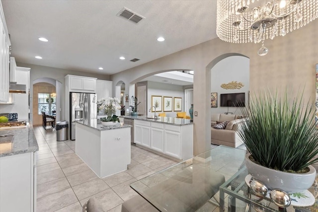 15264 Shonan Gold Dr, Winter Garden, FL 34787 - kitchen with arched walkways, stainless steel appliances, a center island, white cabinets, and light stone counters