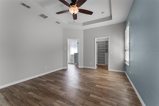 6539 Chagford Ln, Windermere, FL 34786 - unfurnished bedroom featuring a walk in closet, a tray ceiling, multiple windows, and wood finished floors