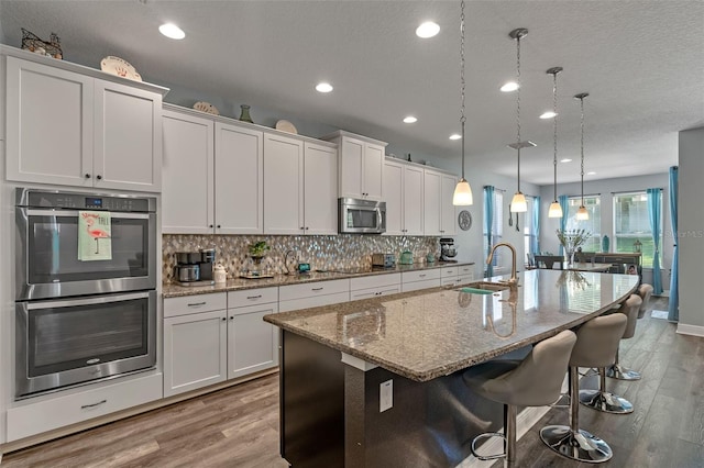1005 Thunderhead Ln, Minneola, FL 34715 - kitchen with appliances with stainless steel finishes, light wood-style floors, backsplash, an island with sink, and recessed lighting
